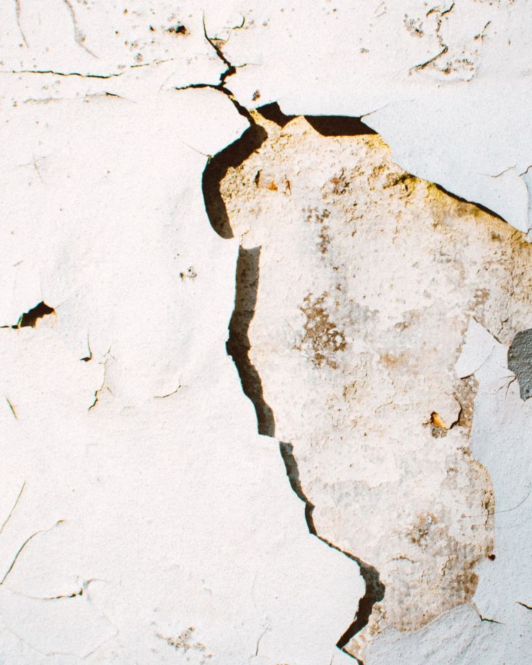 Nahaufnahme eines Risses in einer verputzten Wand mit abblätternder Farbe
